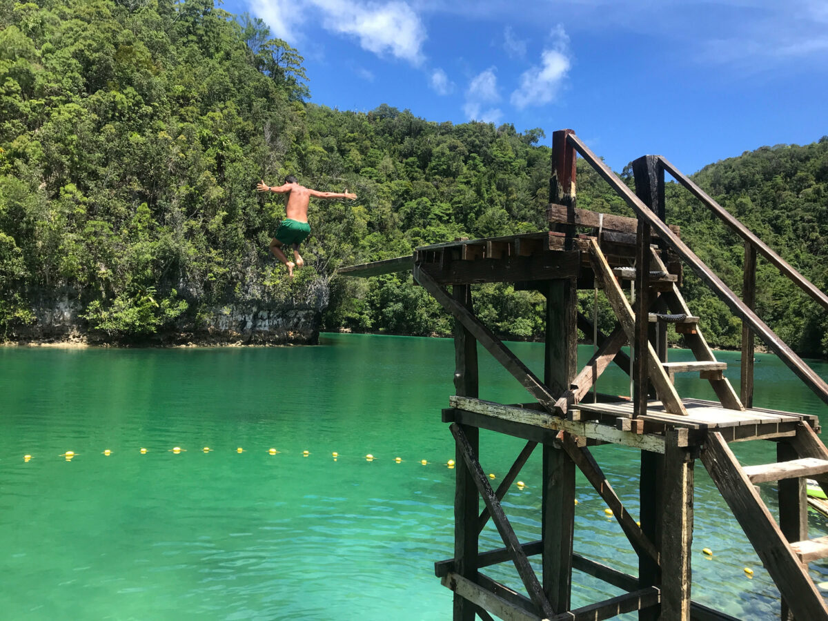 Manolo tirándose de trampolín en un lago con montañas de fondo