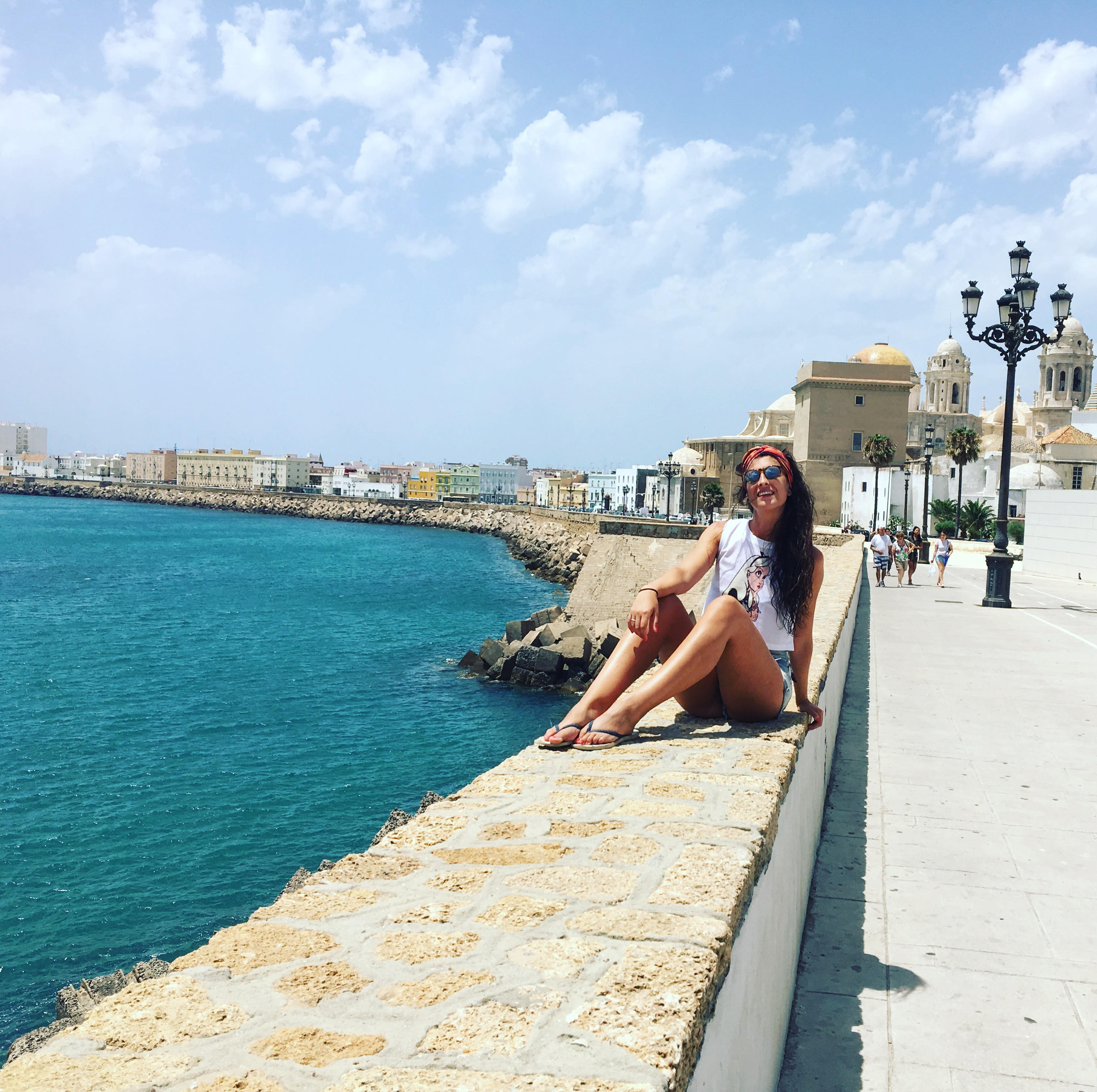 Irene sentada en un muro con el mar a un lado y la catedral de cadiz a otro