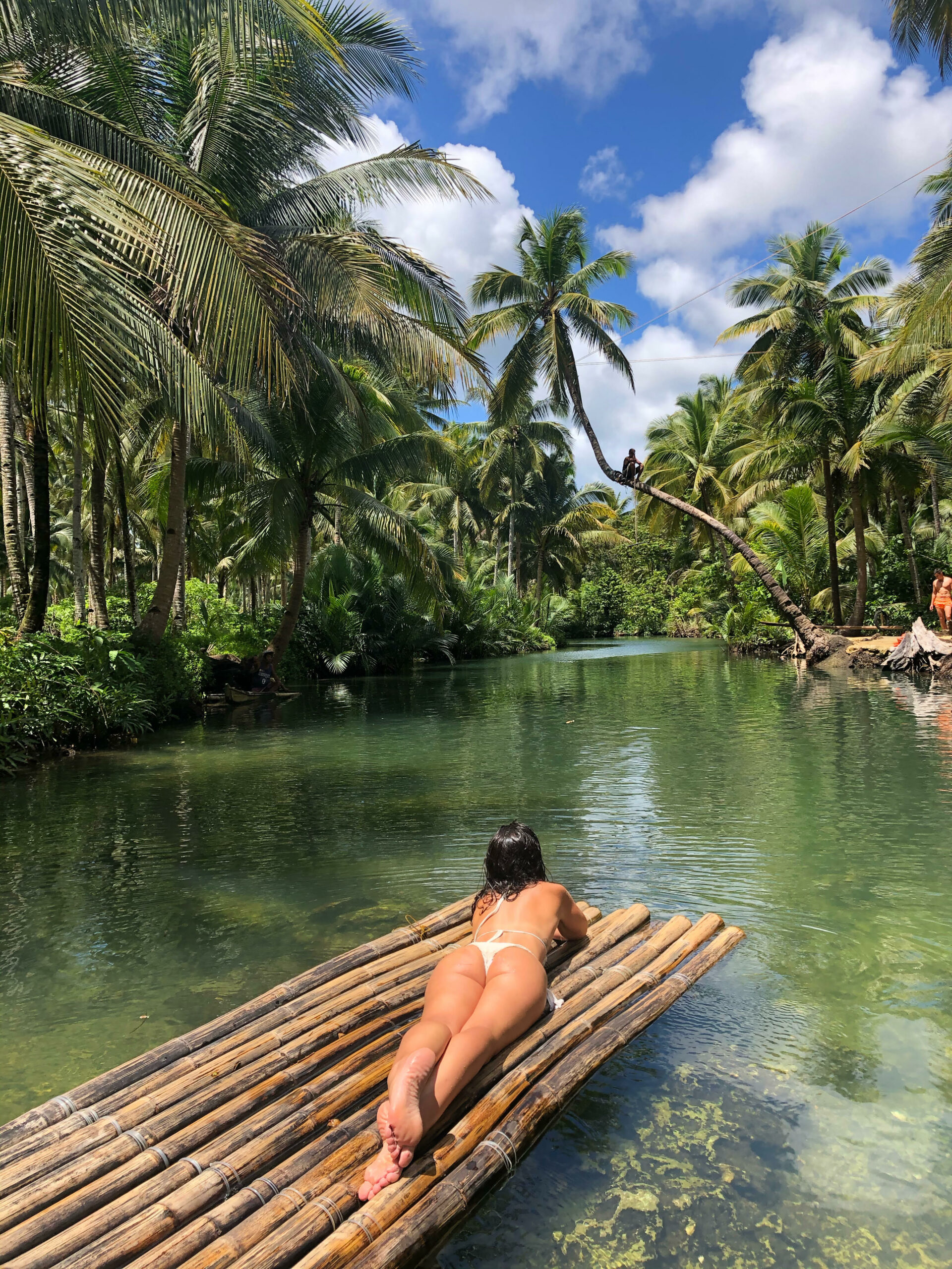 Irene tendida en barca de bambu, en un rio dentro de un palmeral