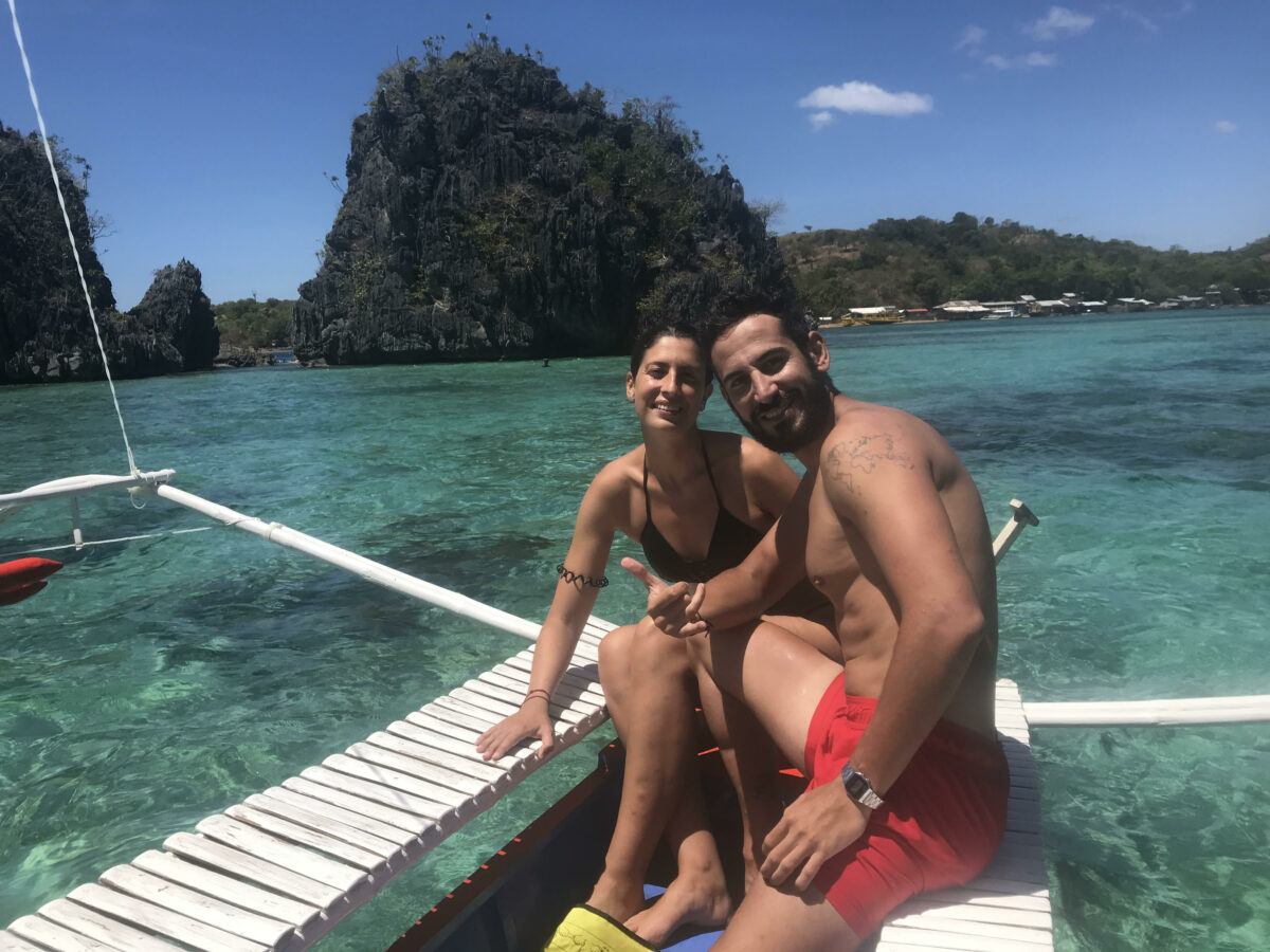 Manolo e Irene en un barco típico filipino con aguas cristalinas y montañas de fondo